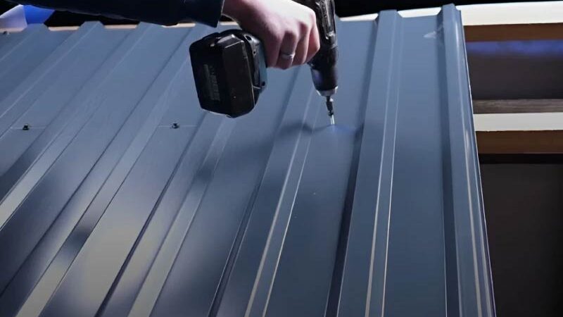 Eine Person verschraubt ein graues Blechdach mit einen Akkuschrauber