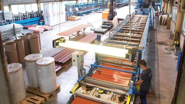 Ein Mitarbeiter bedient eine Maschine zur Herstellung von Dachblechen in einer Fabrikhalle.