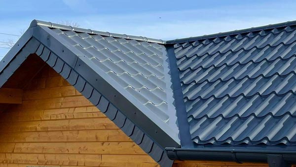 Ein graues Blechdach mit Wellenprofil auf einem Holzhaus vor blauem Himmel