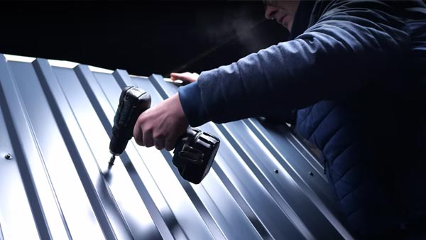 Eine Person verschraubt ein Dachblech mit einem Akkuschrauber